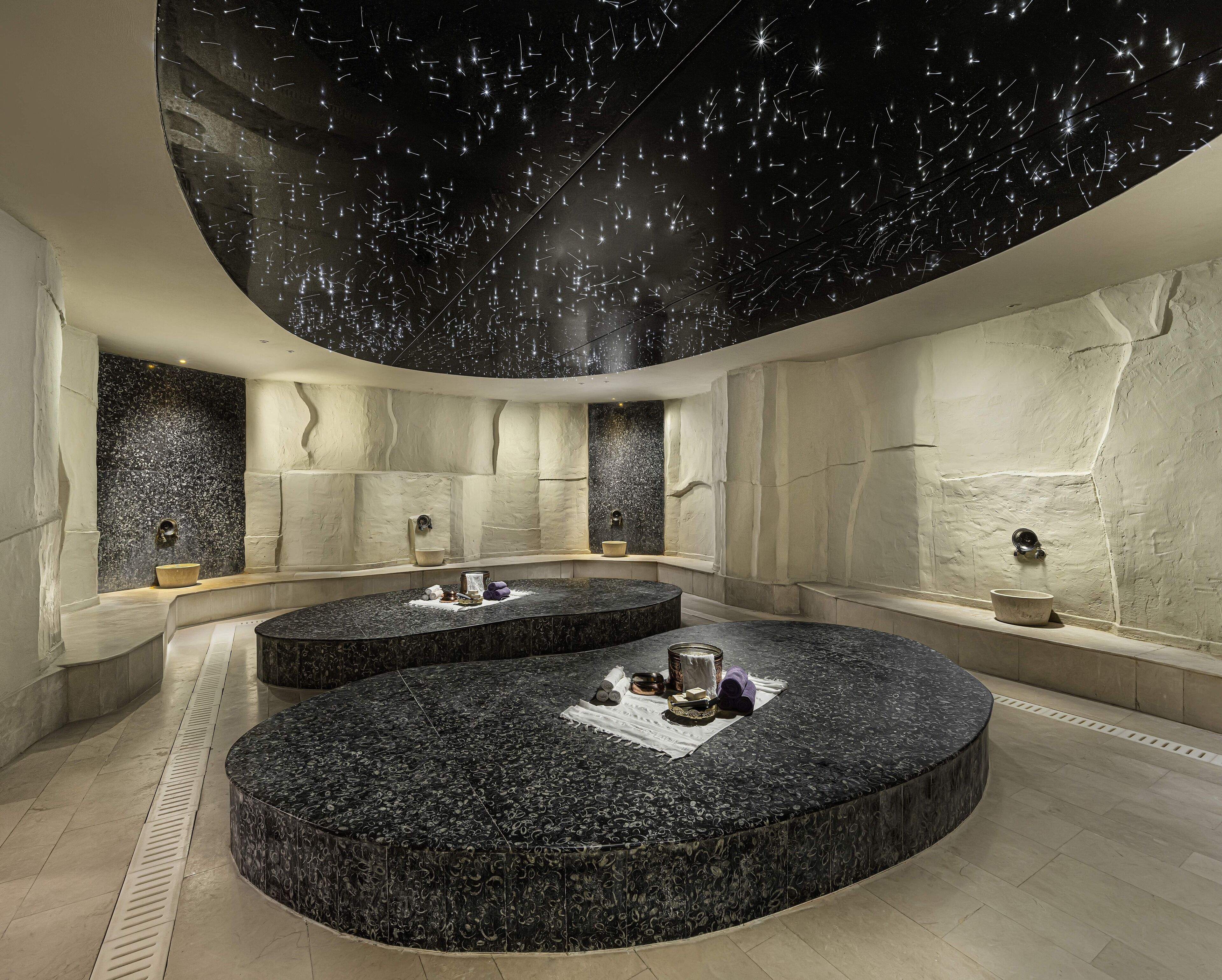 A modern spa with two circular seating areas, a starry ceiling, and a stone wall.