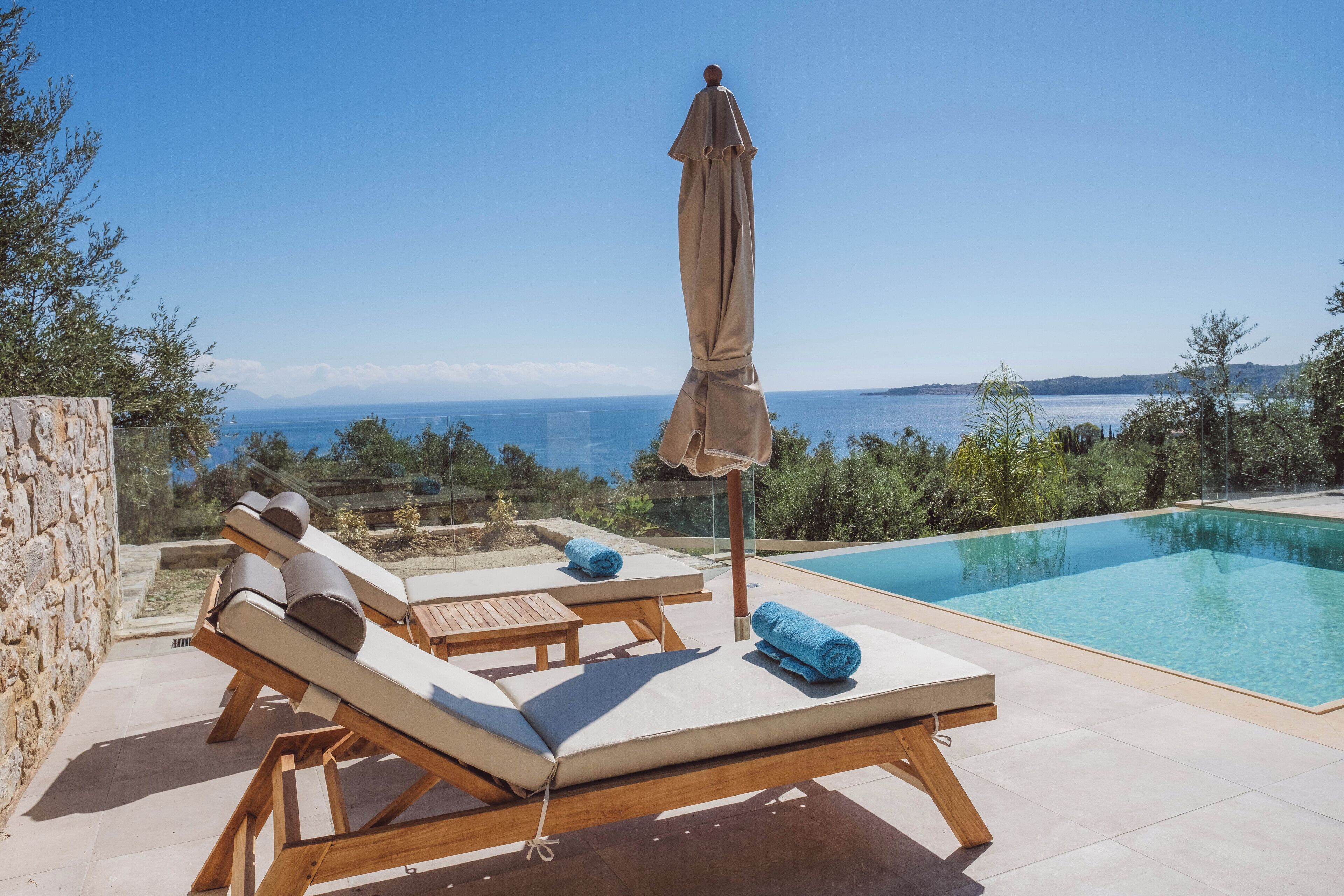 Ein Poolbereich mit Liegestühlen und Sonnenschirm, mit Blick auf das klare, blaue Meer.