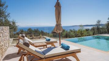 Ein Poolbereich mit Liegestühlen und Sonnenschirm, mit Blick auf das klare, blaue Meer.
