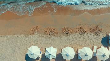 An aerial view of a beach with rows of white umbrellas and lounge chairs, indicating a beachside resort setting.