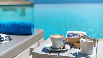 A poolside setting with a cup of coffee, sunglasses, and a book on a wooden table.
