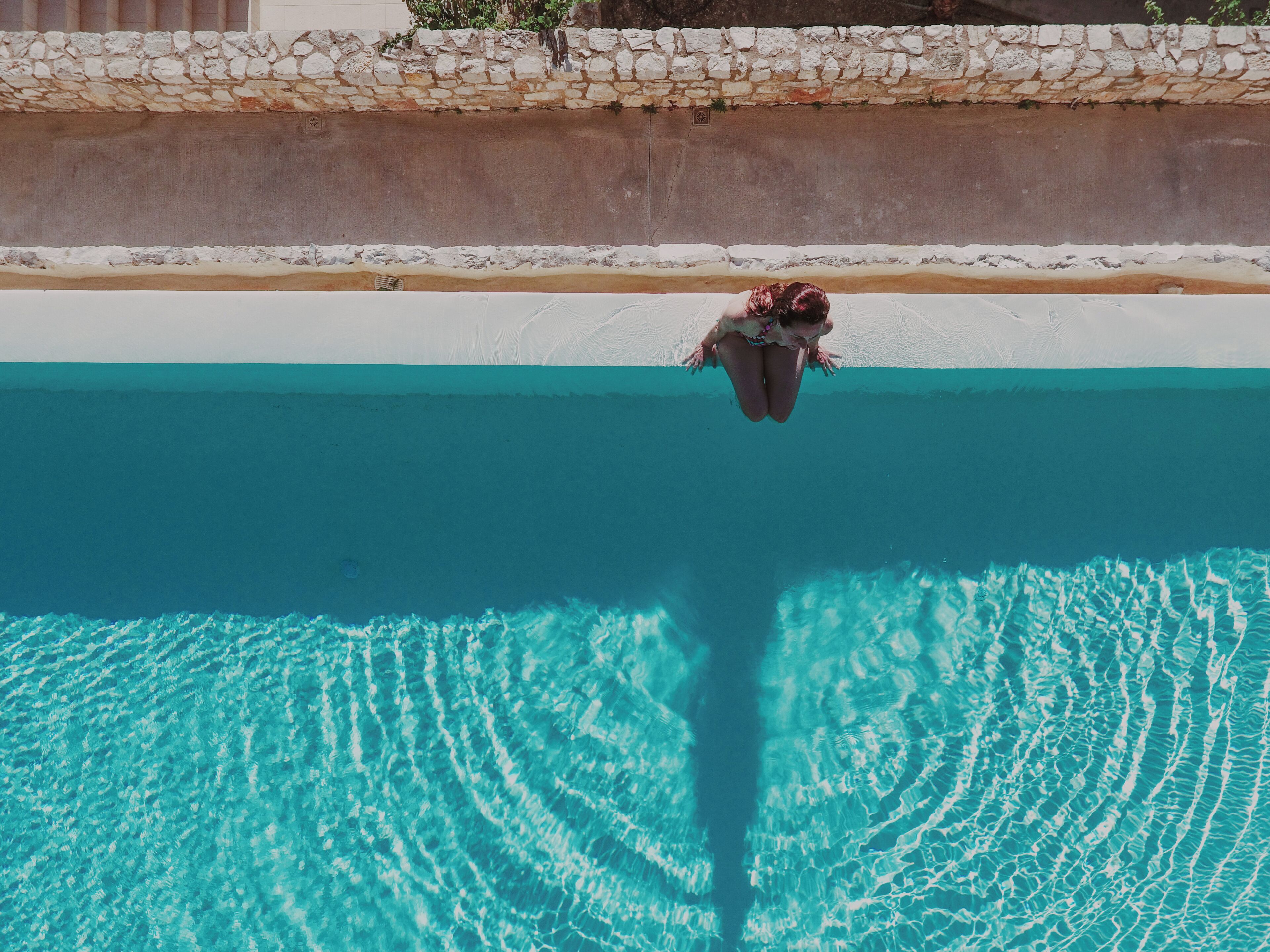 Una persona se sumerge en una piscina azul cristalina, con una pared de piedra y azulejos blancos al fondo.