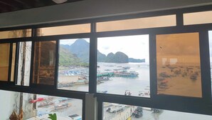 Une vue à travers une fenêtre à carreaux multiples, dévoilant un paysage côtier avec des bateaux et un relief montagneux.