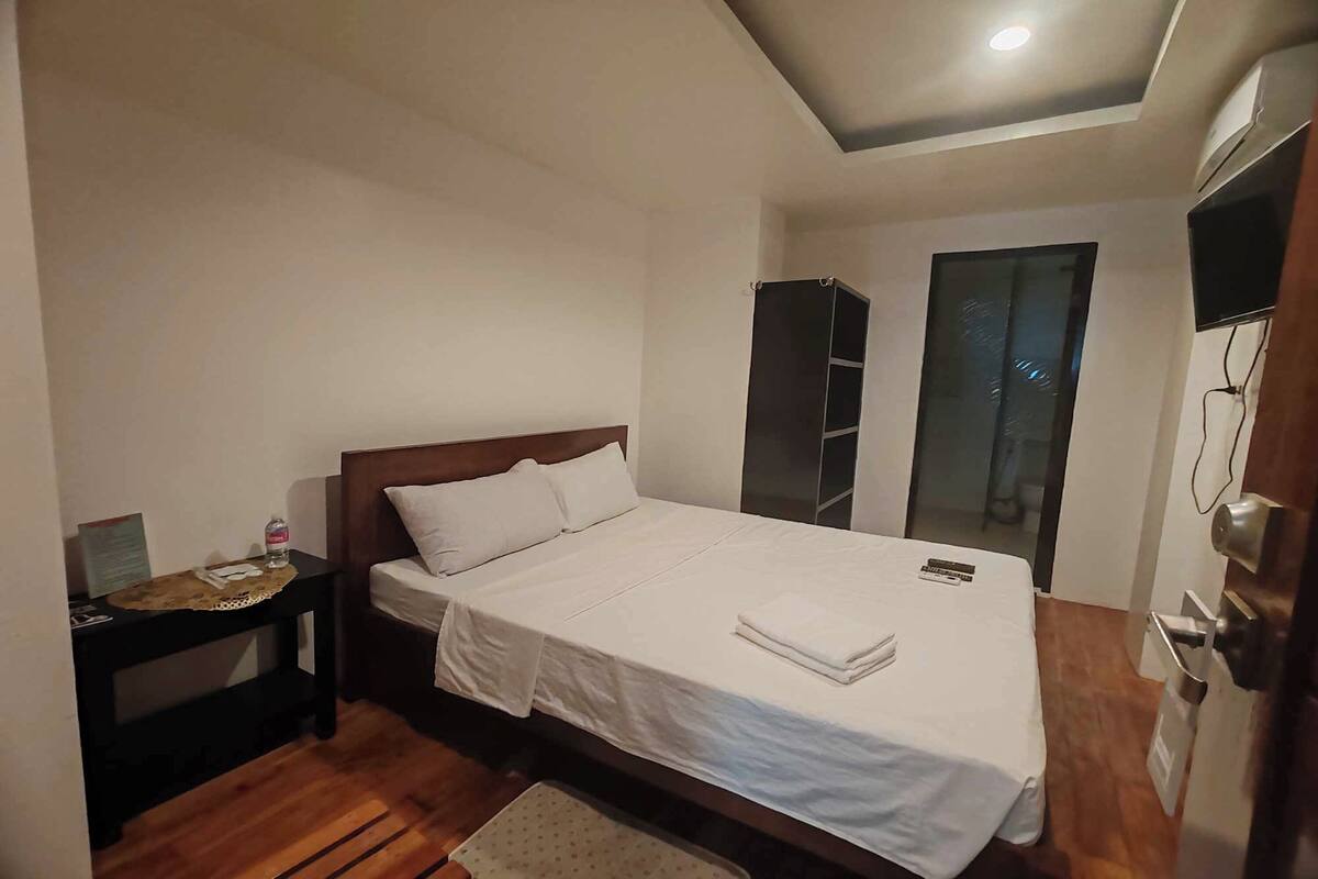 A hotel room with a bed, a nightstand, a desk, a chair, a wardrobe, and a television.