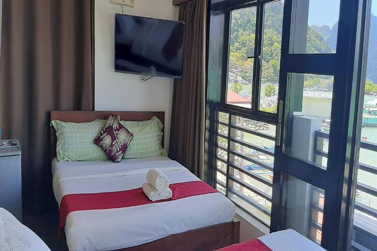 A hotel room with a bed, a TV mounted on the wall, and a window with a view of the outdoors.