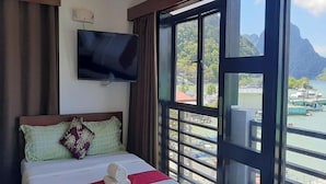 Une chambre d’hôtel avec un lit, un téléviseur fixé au mur et une grande fenêtre donnant sur un plan d’eau et des montagnes.