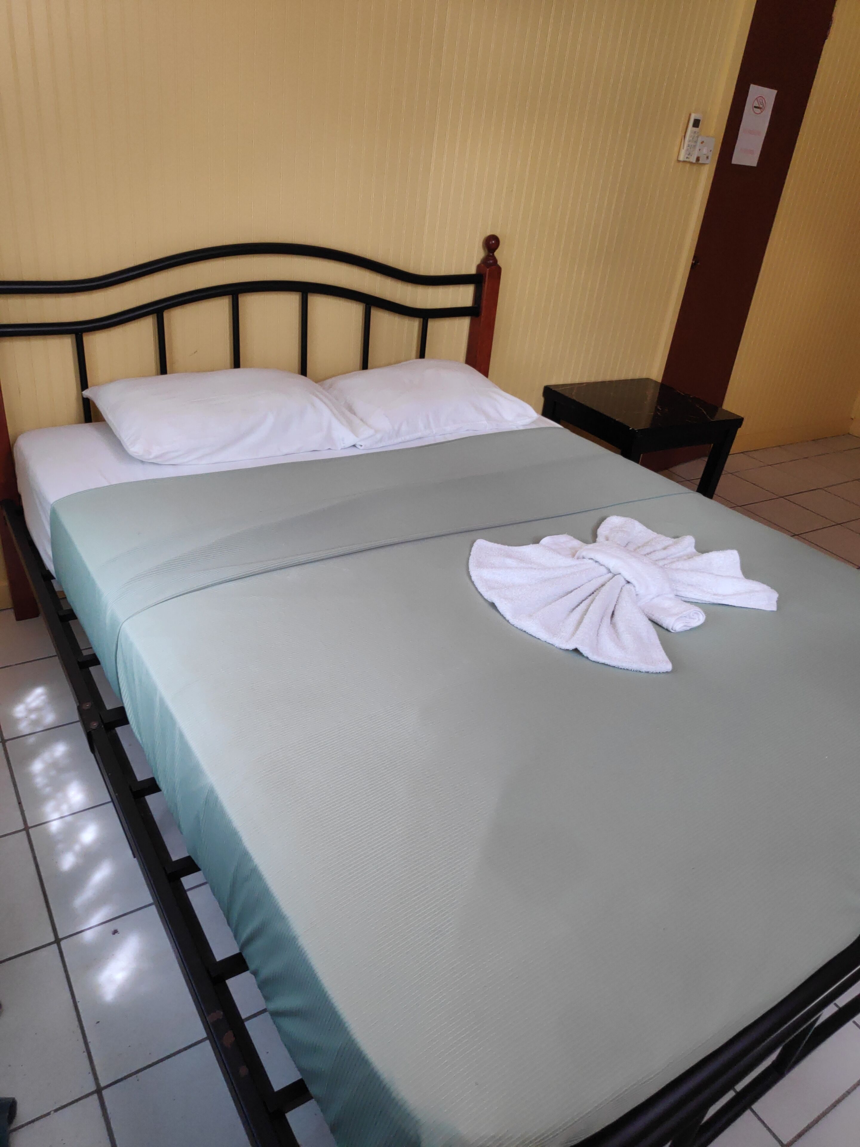 Een net opgemaakt bed met witte kussens en een opgevouwen handdoek op een lichtgroene spreidek.