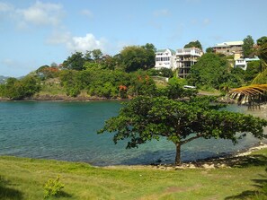 Une zone côtière avec une plage bordée d ’arbres, une vue dégagée sur la mer et des bâtiments en arrière-plan.