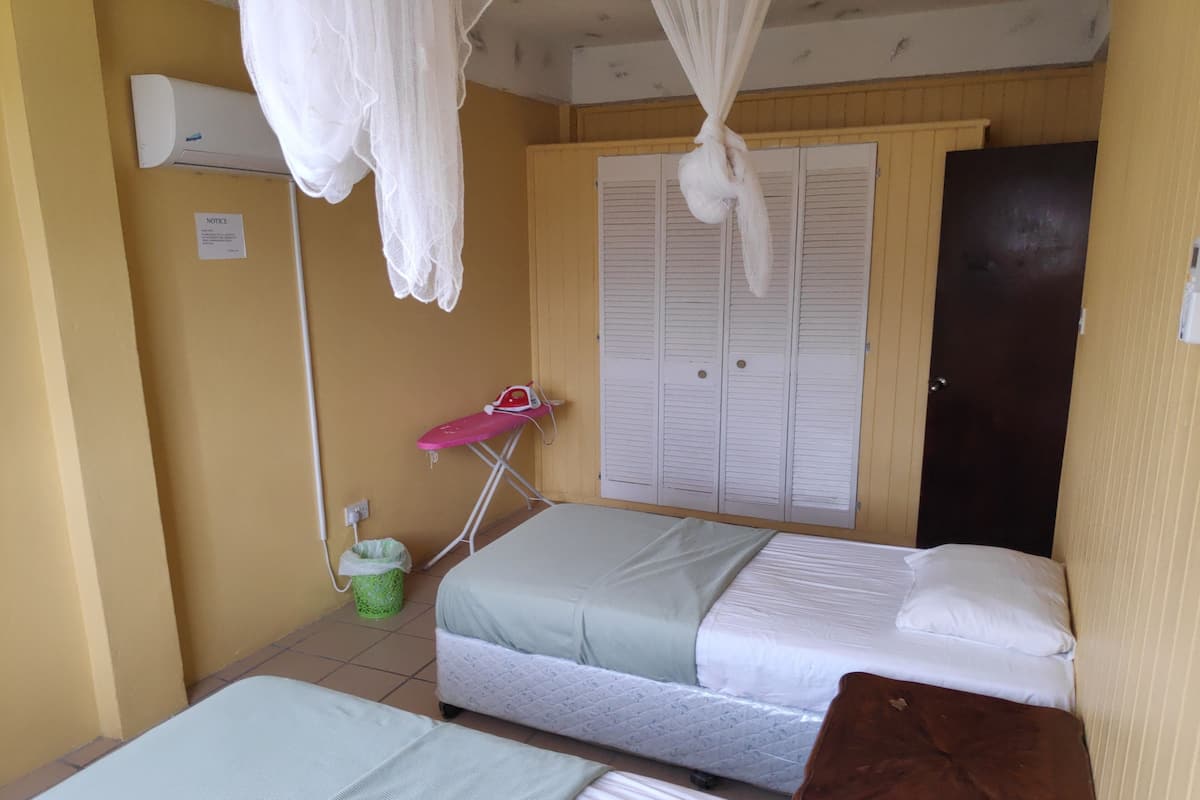 A small, compact room with two single beds, a small table, a pink ironing board, and a wardrobe with multiple doors.