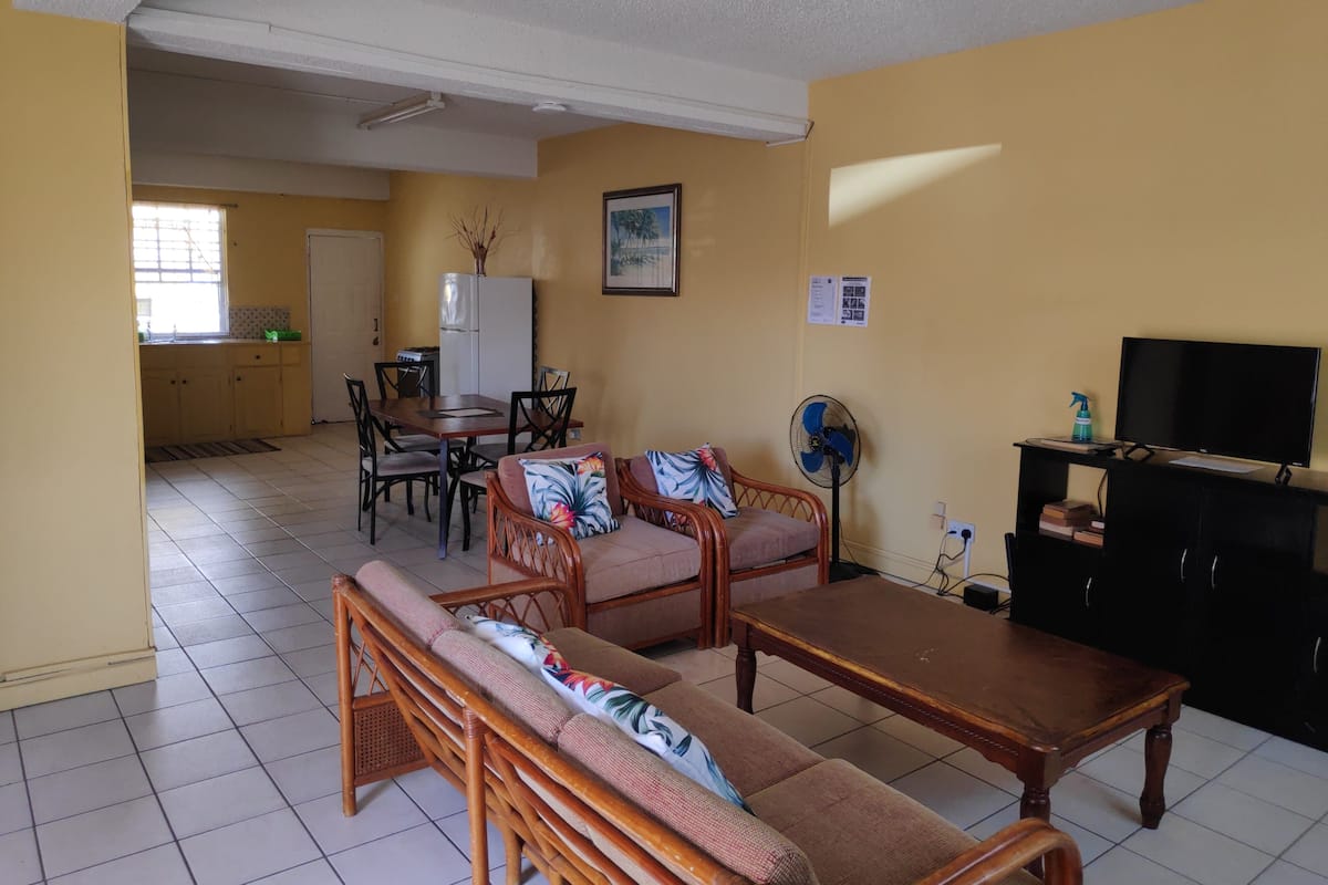 A compact living space with a sofa, dining table, and chairs, a TV, and a fan.