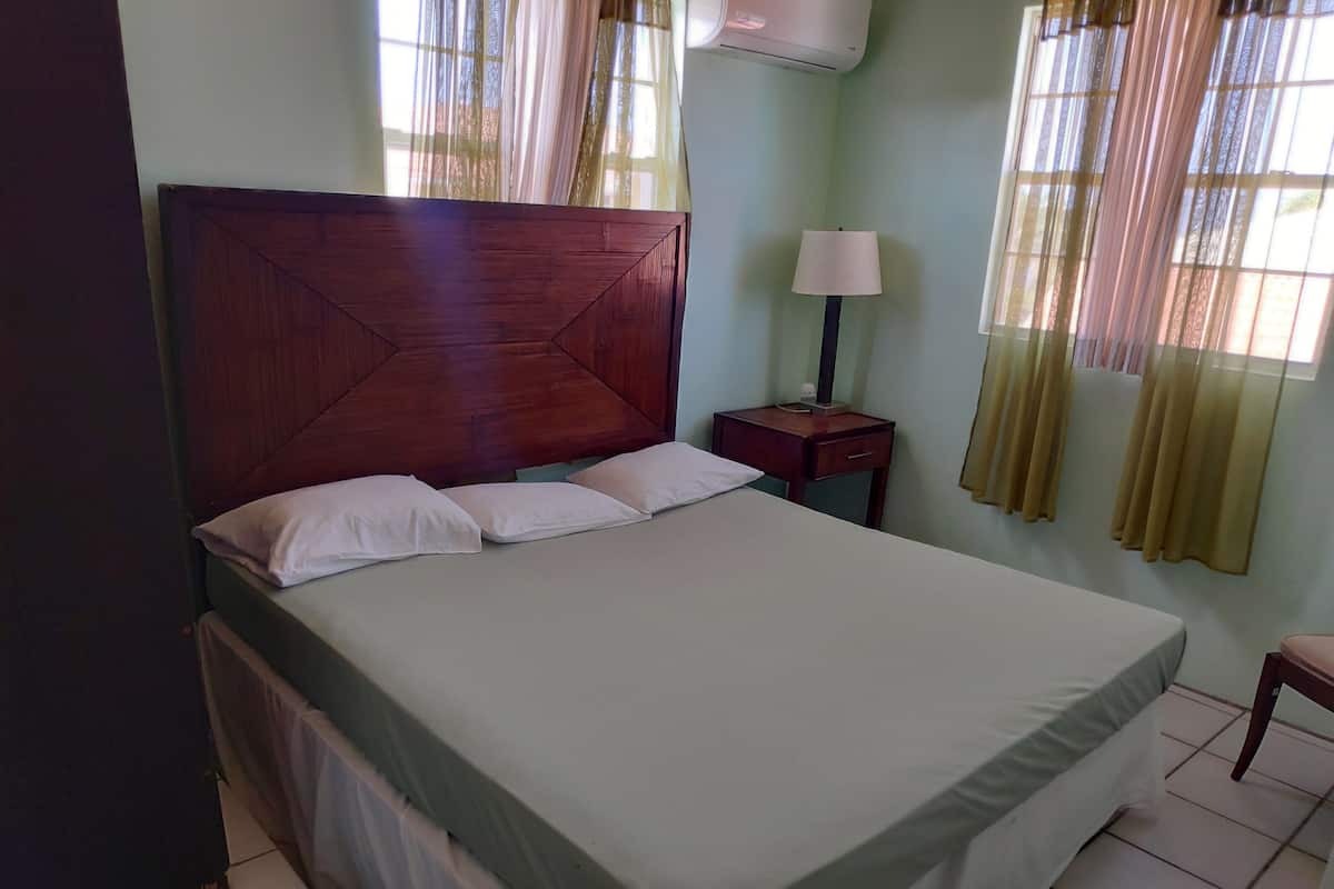 A neatly made bed with a wooden headboard, a bedside table with a lamp, and a window with curtains.