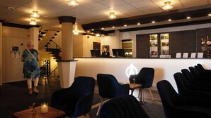 A hotel reception area with a counter, seating, and a staircase.