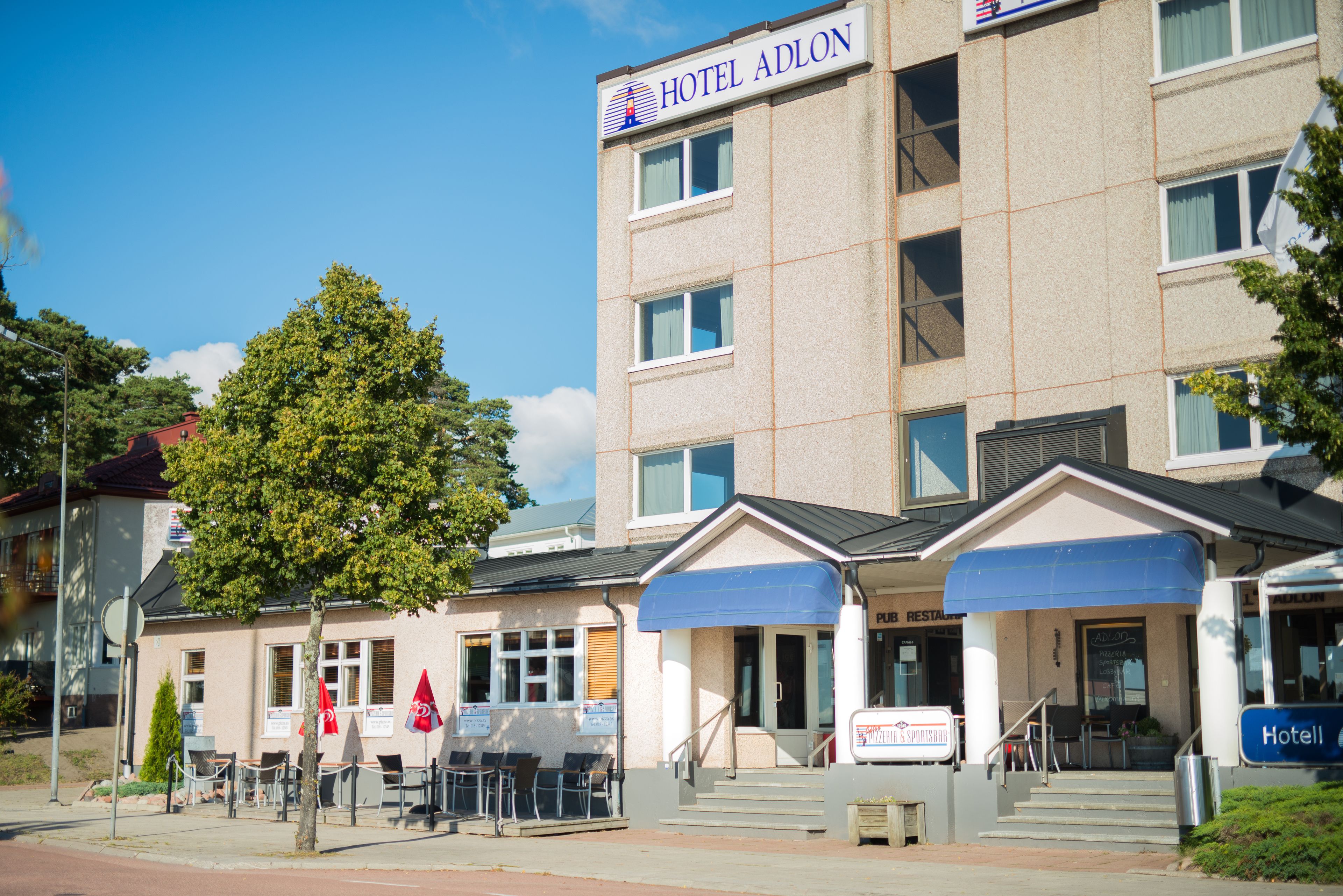 A hotel with a sign reading "HOTEL ADLON," a public restaurant, and outdoor seating with chairs and tables.