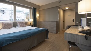 A hotel room with a bed, bedside table, lamp, and a desk with a phone and glasses.