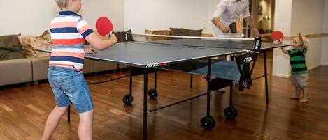 A ping pong table in a room with wooden flooring and a sofa in the background.