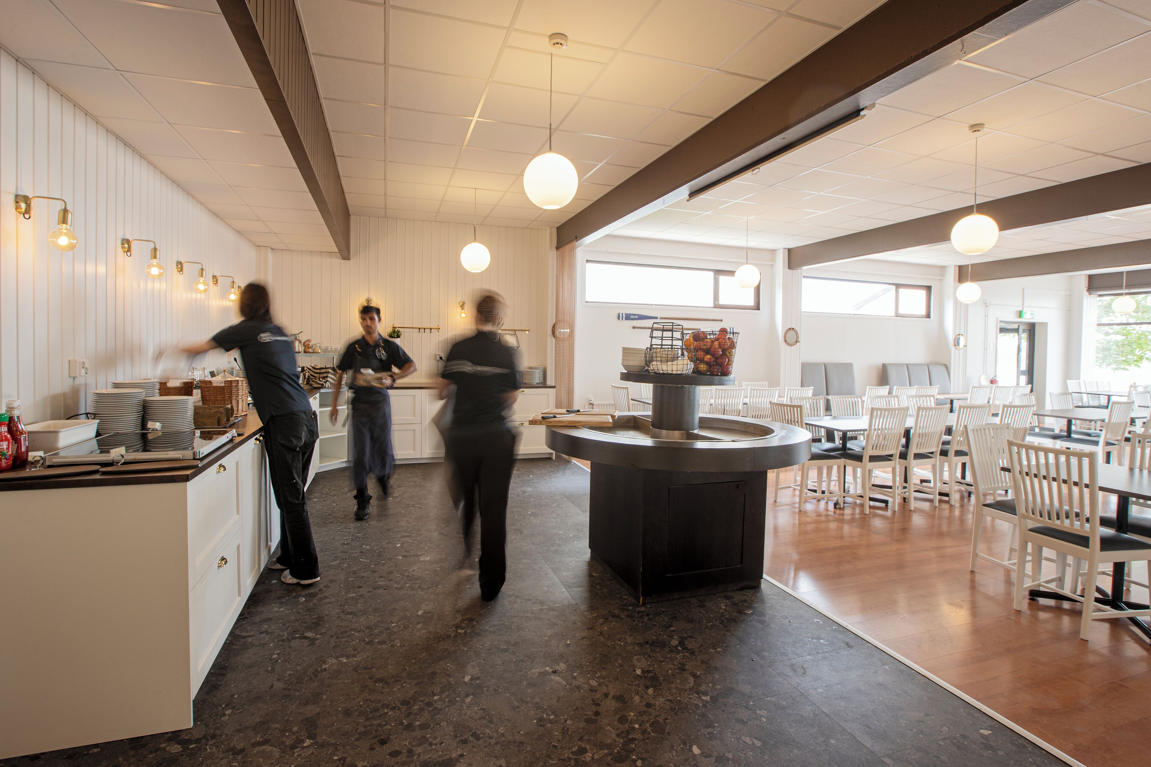 A spacious restaurant with a central island, white walls, and a mix of seating arrangements.