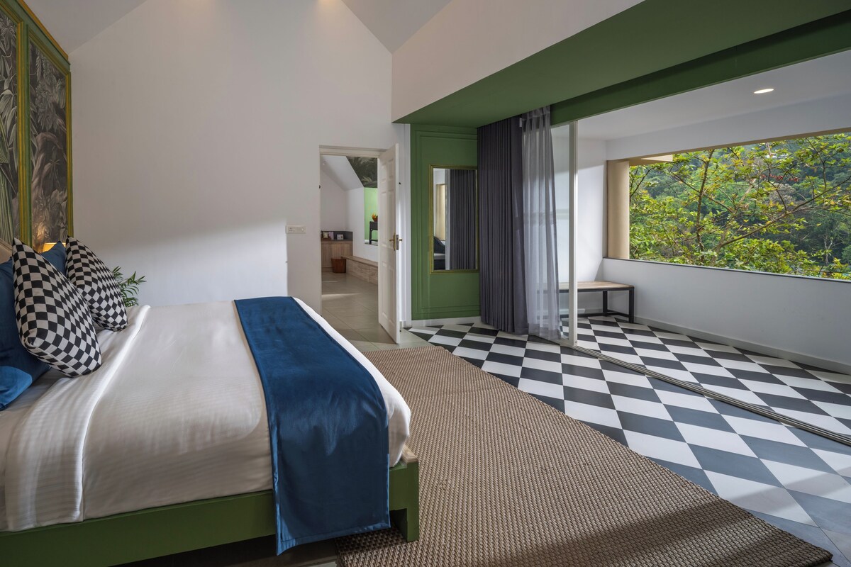 Un dormitorio moderno con cama, piso de cuadros, un ventanal con vistas y una pared verde decorativa.