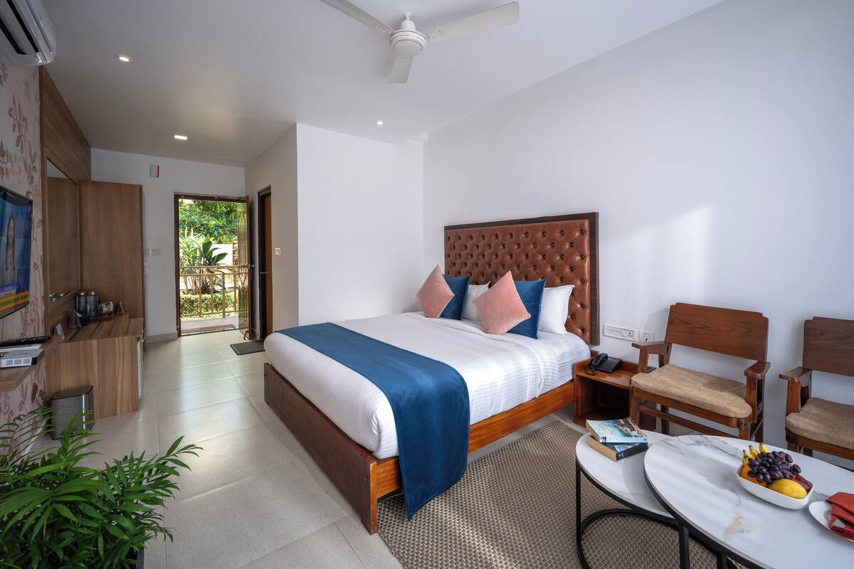 Habitación de hotel moderna con una cama grande, cabecera de madera, un escritorio con silla, una mesita con fruta y vistas al exterior.