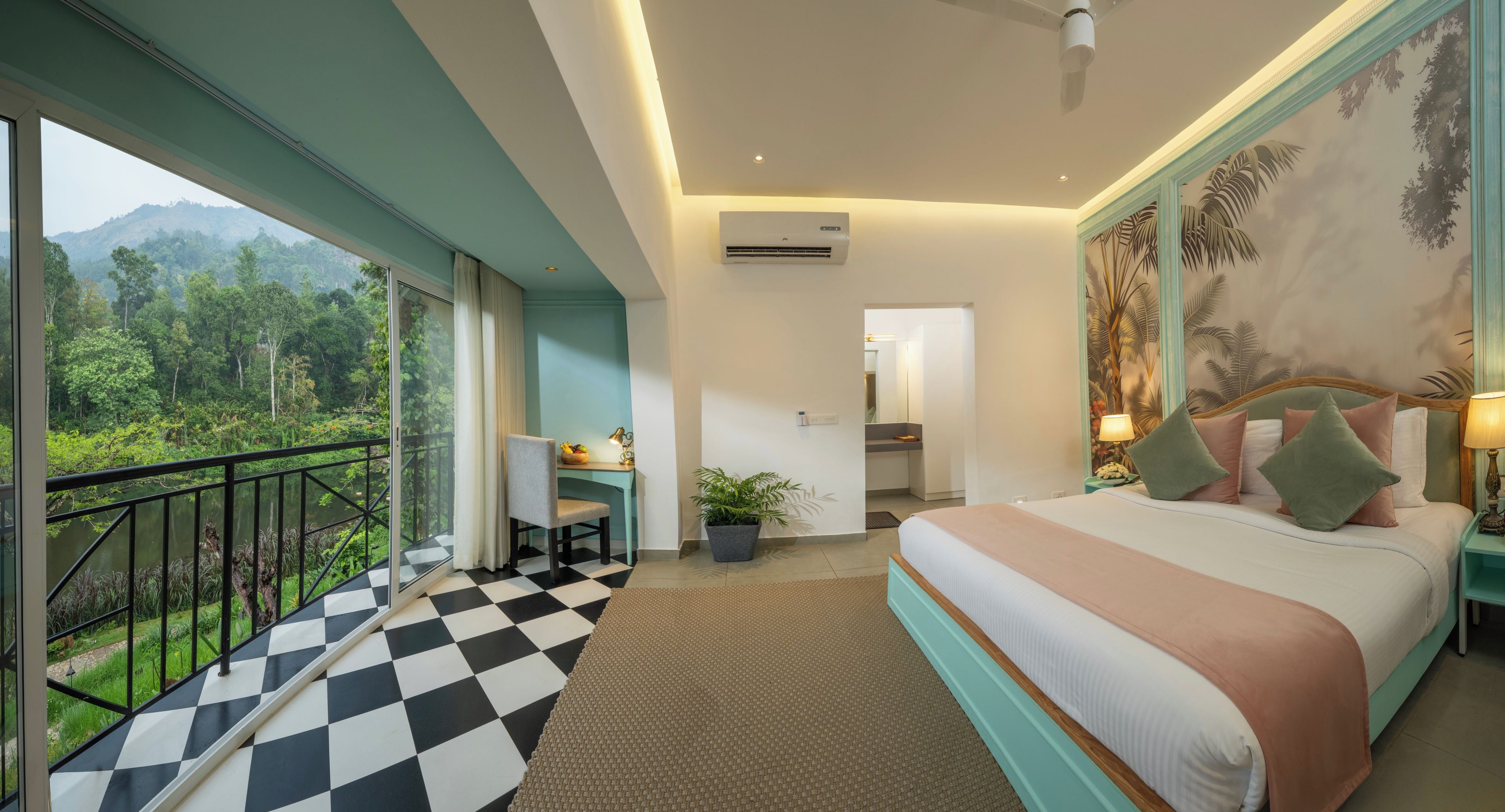 Une chambre d’hôtel avec un balcon, un sol à carreaux, un lit avec des oreillers et une fresque murale aux motifs tropicaux.