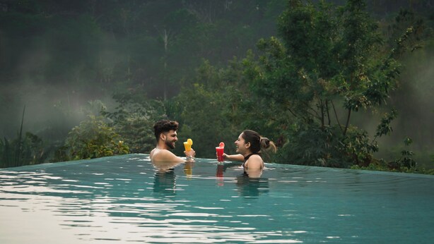 Un couple se trouve dans une piscine aux eaux claires et paisibles, avec une végétation luxuriante en arrière-plan.