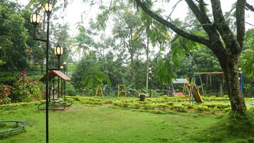 Explore a serene park setting with a playground featuring a swing set, slide, and small bridge over a water feature, surrounded by lush greenery and trees.