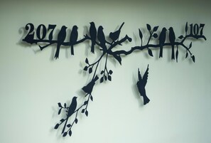 Una obra de arte mural con siluetas de pájaros en ramas y los números '207' y '107'.
