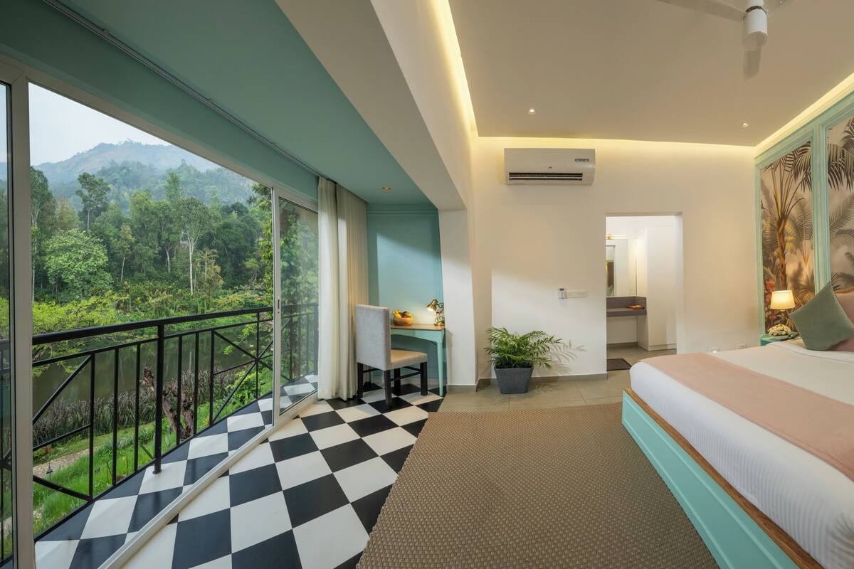 Habitación de hotel con balcón, suelo a cuadros, cama con almohadas y un mural tropical.