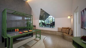 Un intérieur moderne avec un banc vert, un canapé, une table à manger dressée et une grande fenêtre offrant une vue dégagée.