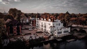 A large white building with multiple stories and a prominent tower, situated by a river with a bridge and a small boat dock. - Thames Riviera Hotel, Sure Hotel Collection by Best Western (Maidenhead)