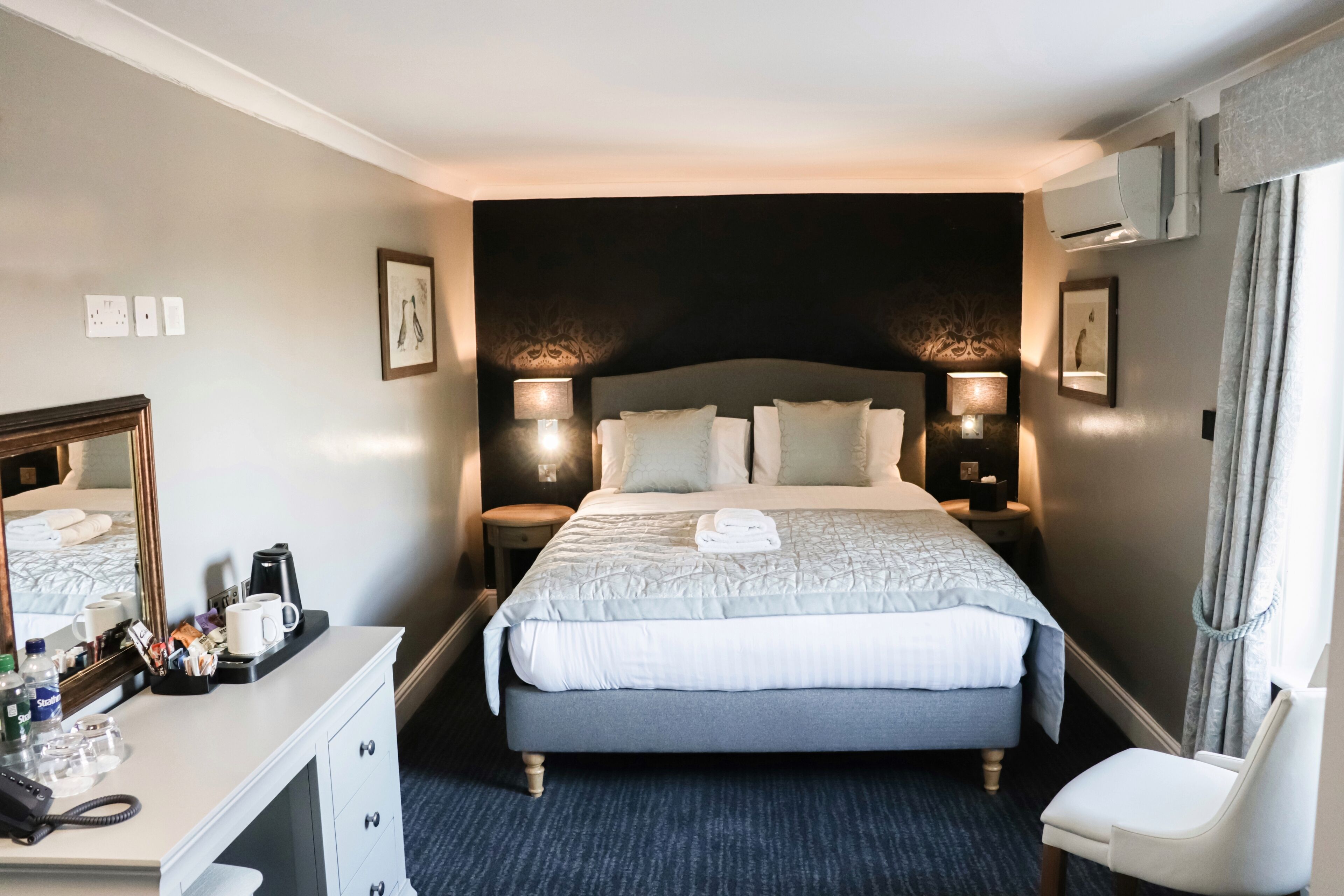 A hotel room with a large bed, bedside lamps, a desk with a phone, and a chair.