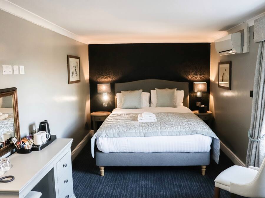 A hotel room with a large bed, bedside lamps, a desk with a phone, and a chair.