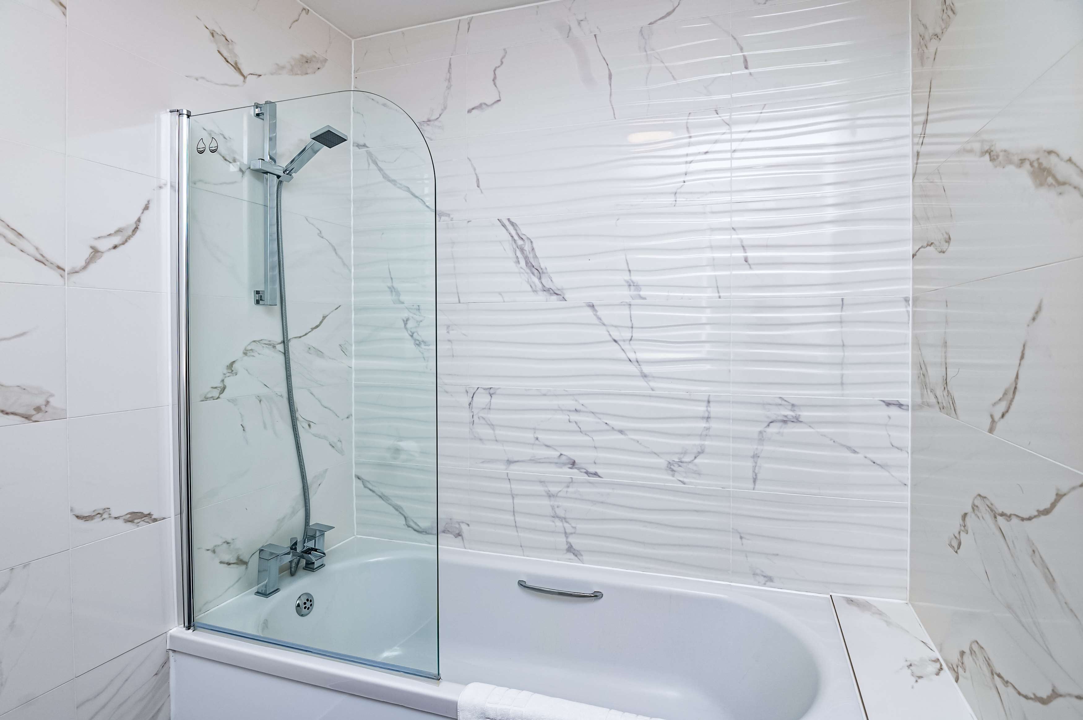 Ein modernes Badezimmer mit einer gläsernen Duschkabine, einer freistehenden Badewanne und Wänden mit Marmoroptik.