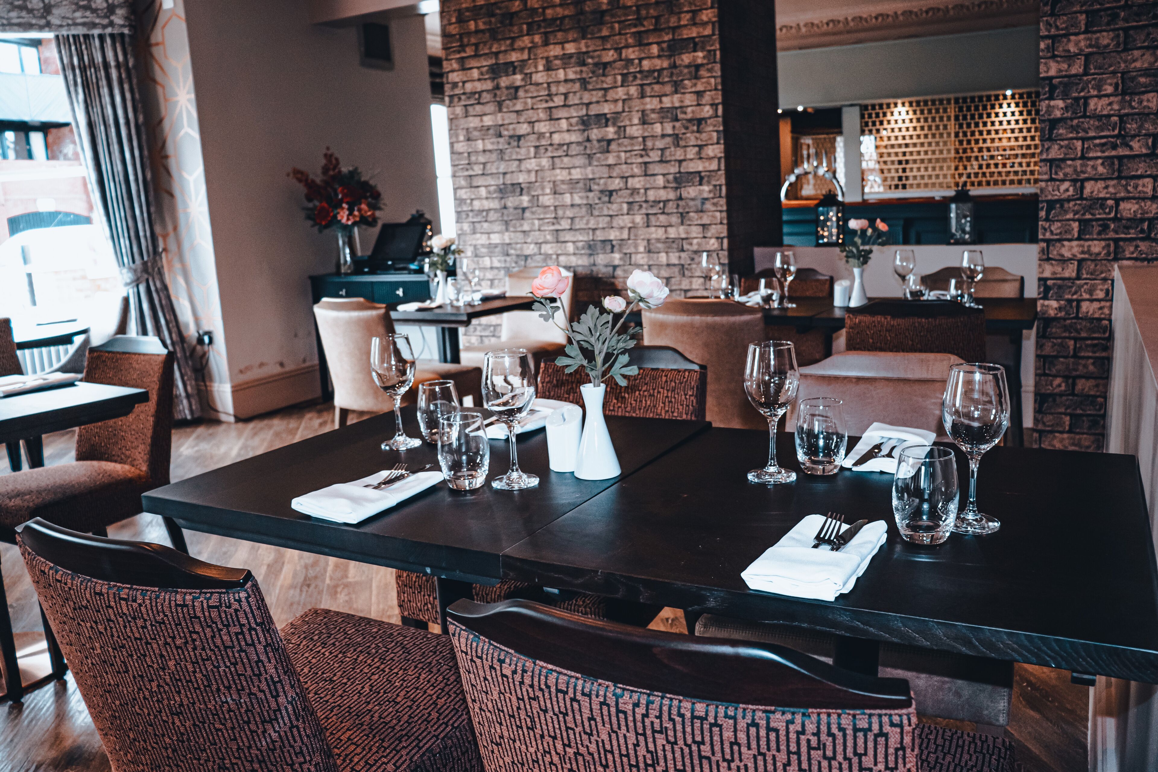 Un restaurante con pared de ladrillo, mesas de madera y sillas estampadas.