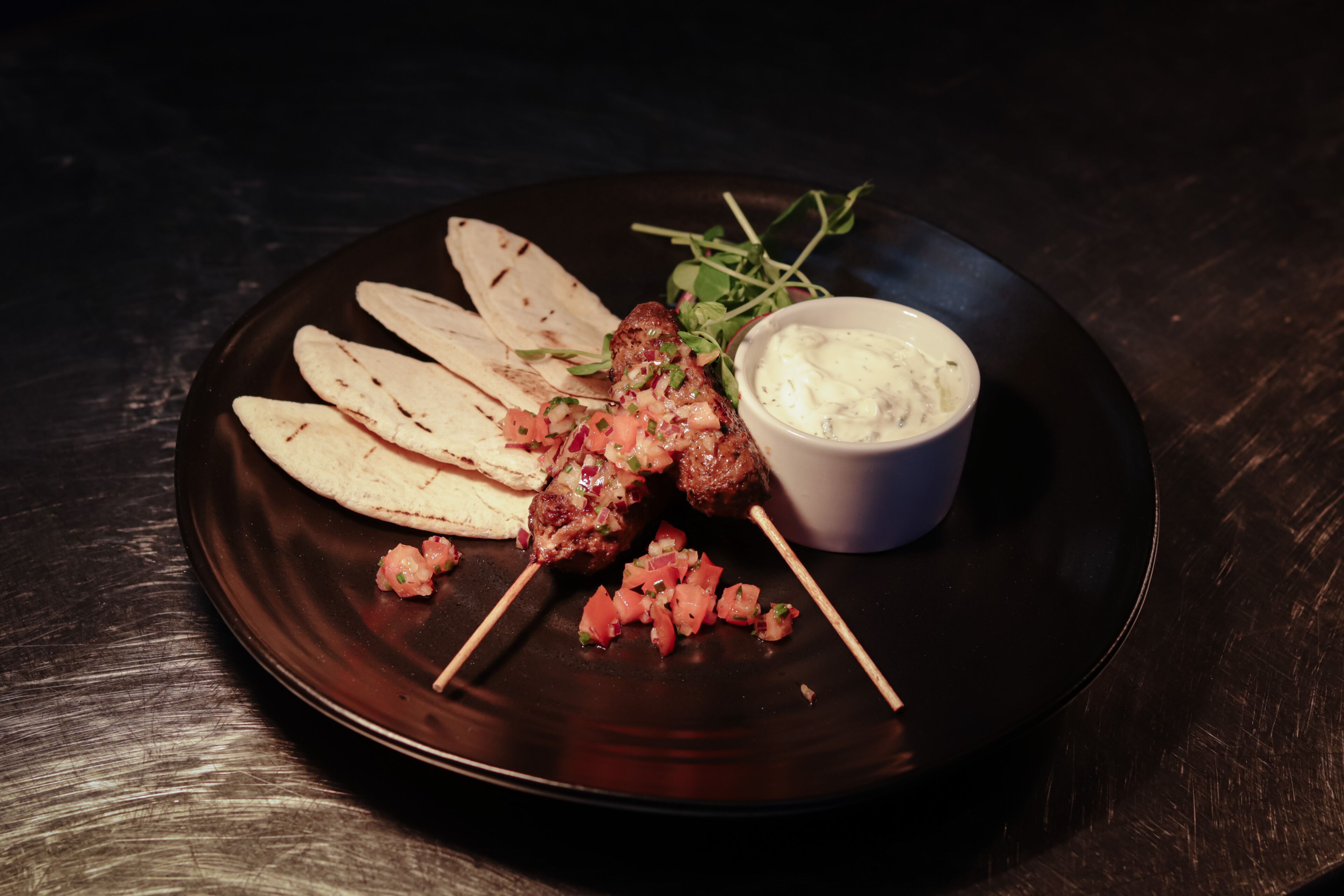 A plate with grilled meat skewers, flatbread, and a small bowl of sauce.