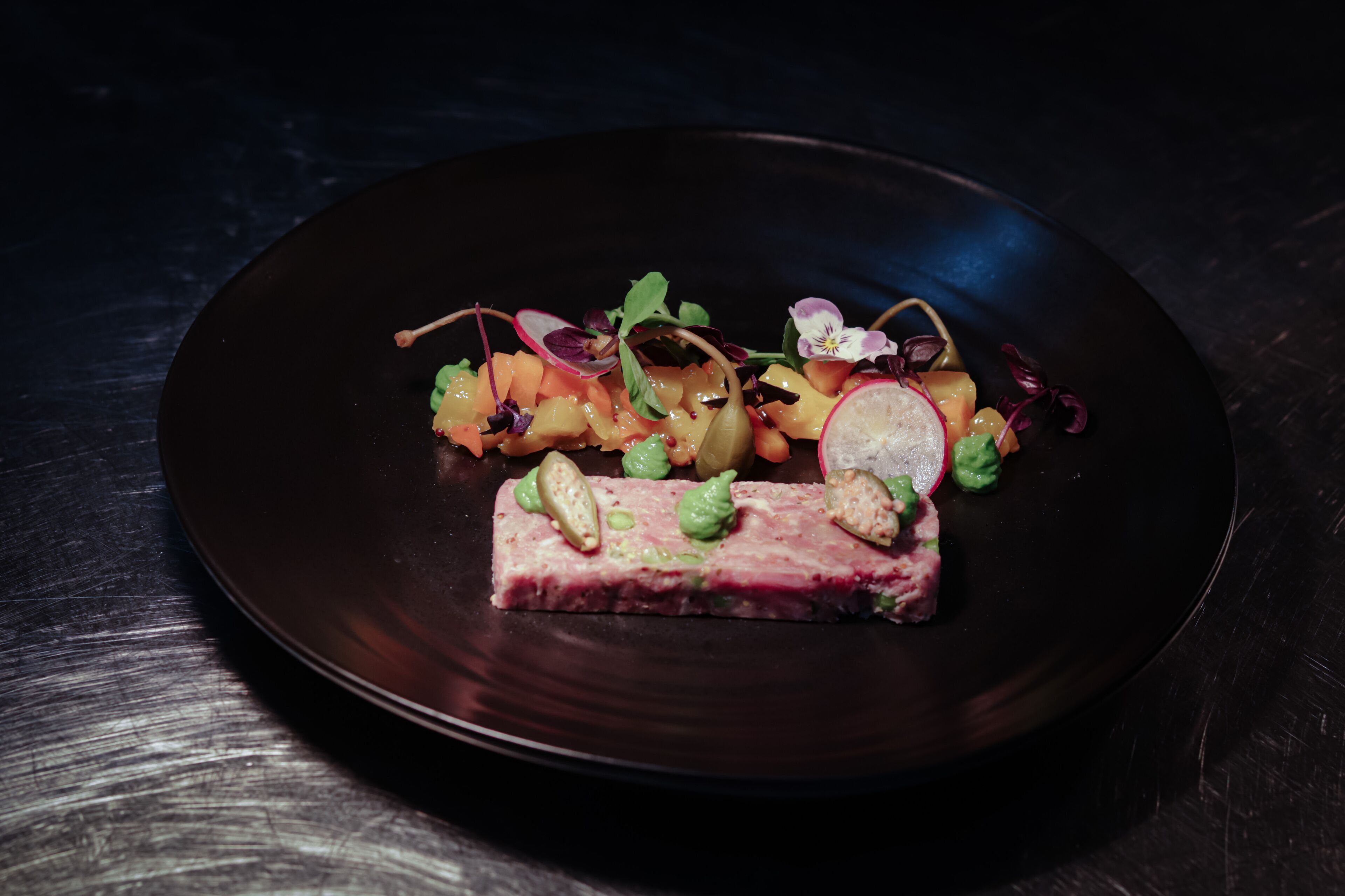 A dark plate with a meat dish and a colorful salad.