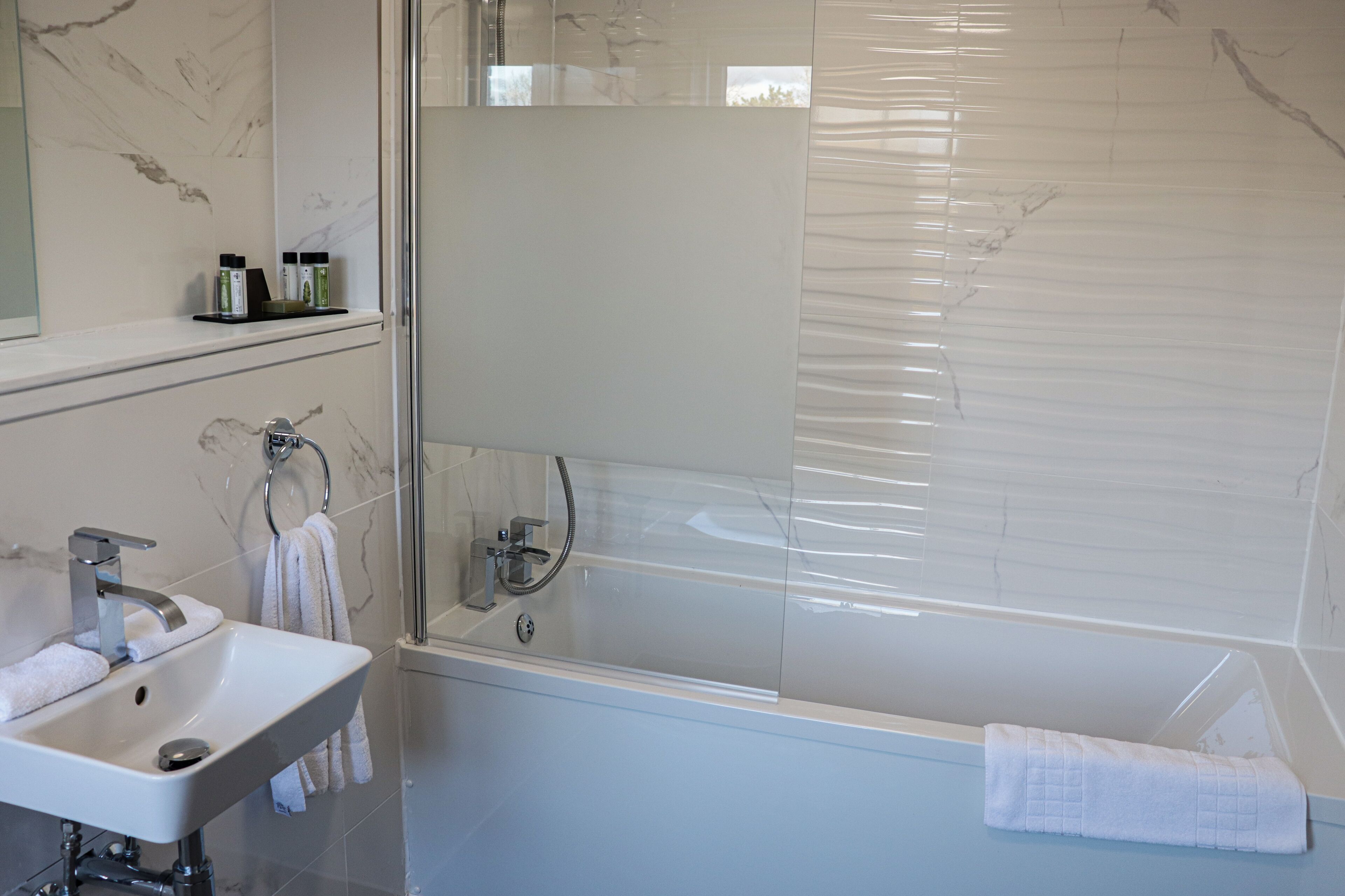 A modern bathroom with a white sink, a glass-enclosed shower, and a marble-tiled wall.