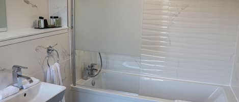 A modern bathroom with a white sink, a glass-enclosed shower, and a marble-tiled wall.