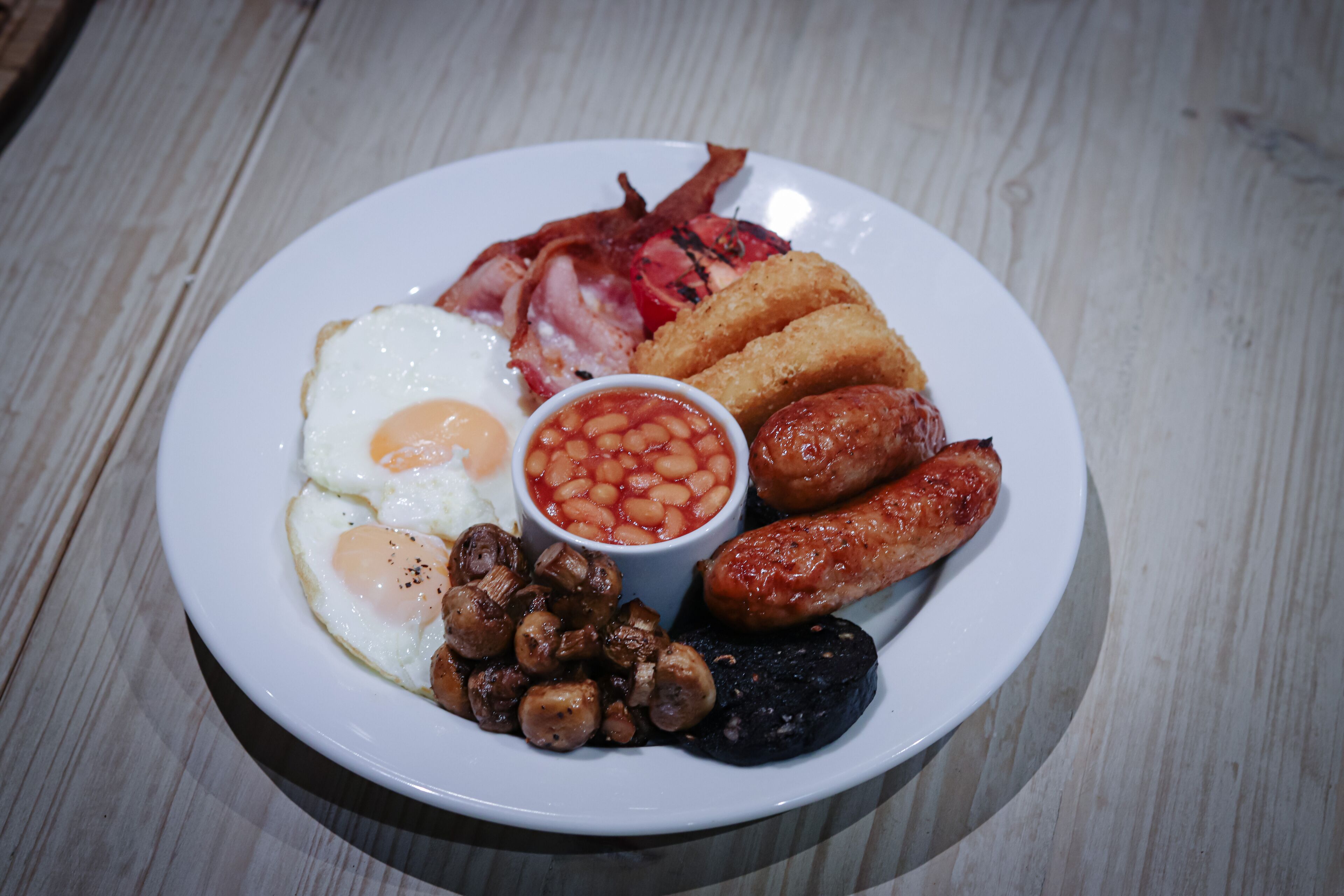 Une assiette de nourriture pour le petit-déjeuner comprenant des œufs, des saucisses, du bacon, des champignons et des haricots cuits.