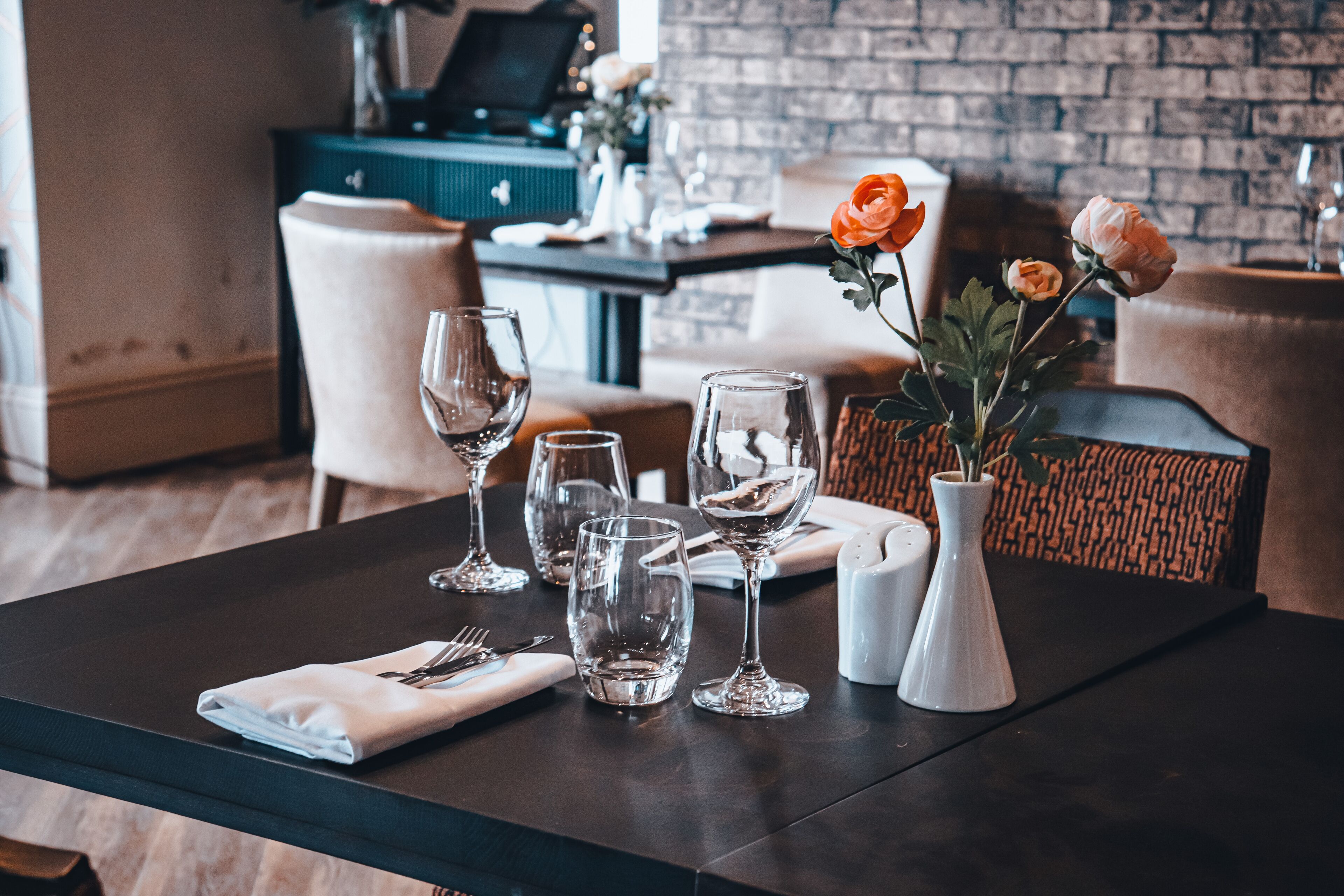 Una mesa de comedor dispuesta con copas de vino, un jarrón con flores y una servilleta doblada sobre la mesa.