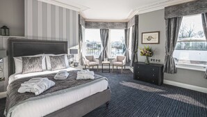 A hotel room with a large bed, two armchairs, a small table, and a view of the city through large windows. - Thames Riviera Hotel, Sure Hotel Collection by Best Western (Maidenhead)
