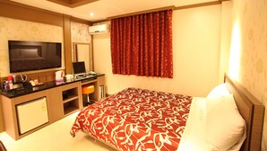 A hotel room with a bed, a desk with a computer, a TV, and a small refrigerator. - Morice Hotel (Gwangyang)
