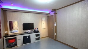 A hotel room with a flat-screen TV, a small desk with a chair, a minibar, and a door leading to another room. - Morice Hotel (Gwangyang)