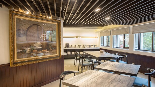 A restaurant with wooden paneling, a large framed painting, and modern lighting. Tables and chairs are arranged for dining. - Rainbow Hotel (Taipei)