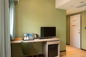 A hotel room with a desk, a flat-screen TV, a chair, a mini-fridge, and a door with a map on it.