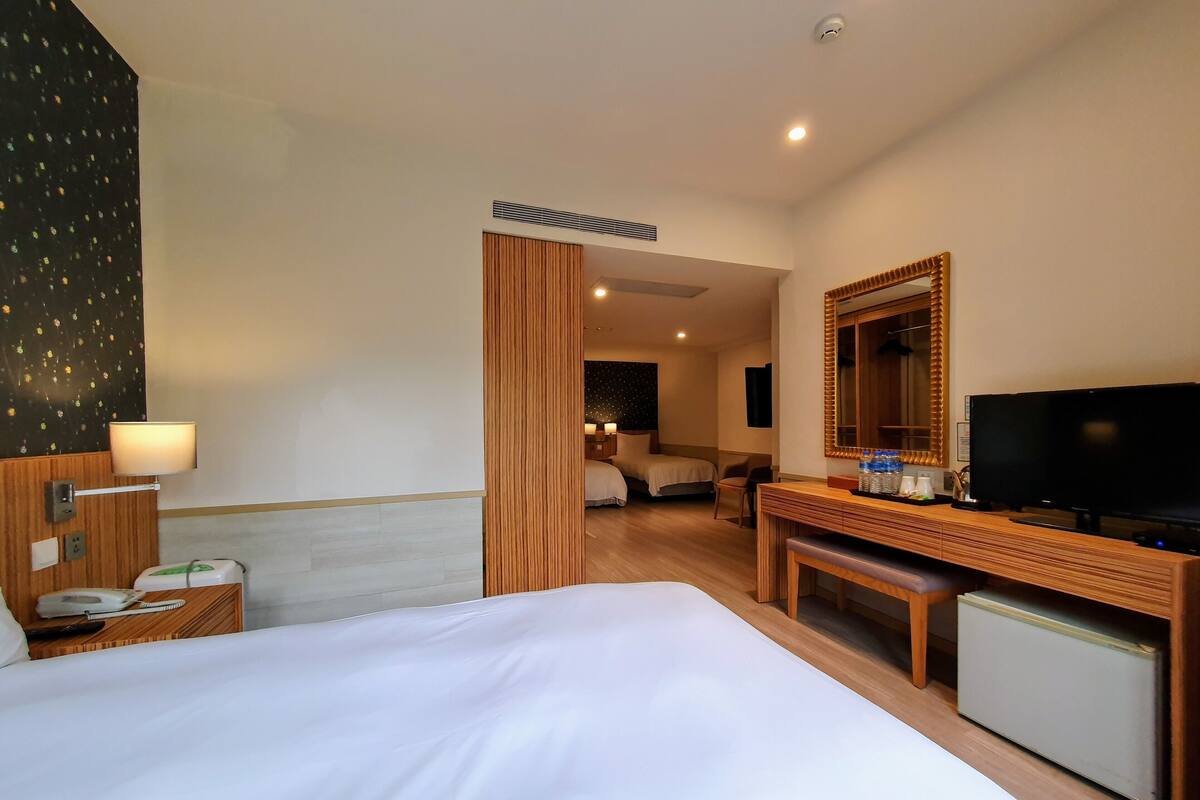 A hotel room with a large bed, a desk with a TV, and a small refrigerator.