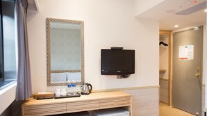 A hotel room with a wooden desk, a television, a small refrigerator, and a mirror with a patterned frame. - Rainbow Hotel (Taipei)