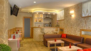 A cozy living area with a sofa, a coffee table, and a small kitchen area with a counter and a stove. - Hotel Belvedere (Roccaraso)
