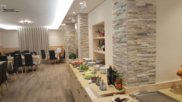 A modern dining area with a stone accent wall, a buffet setup, and a separate dining table with chairs. - Hotel Belvedere (Roccaraso)