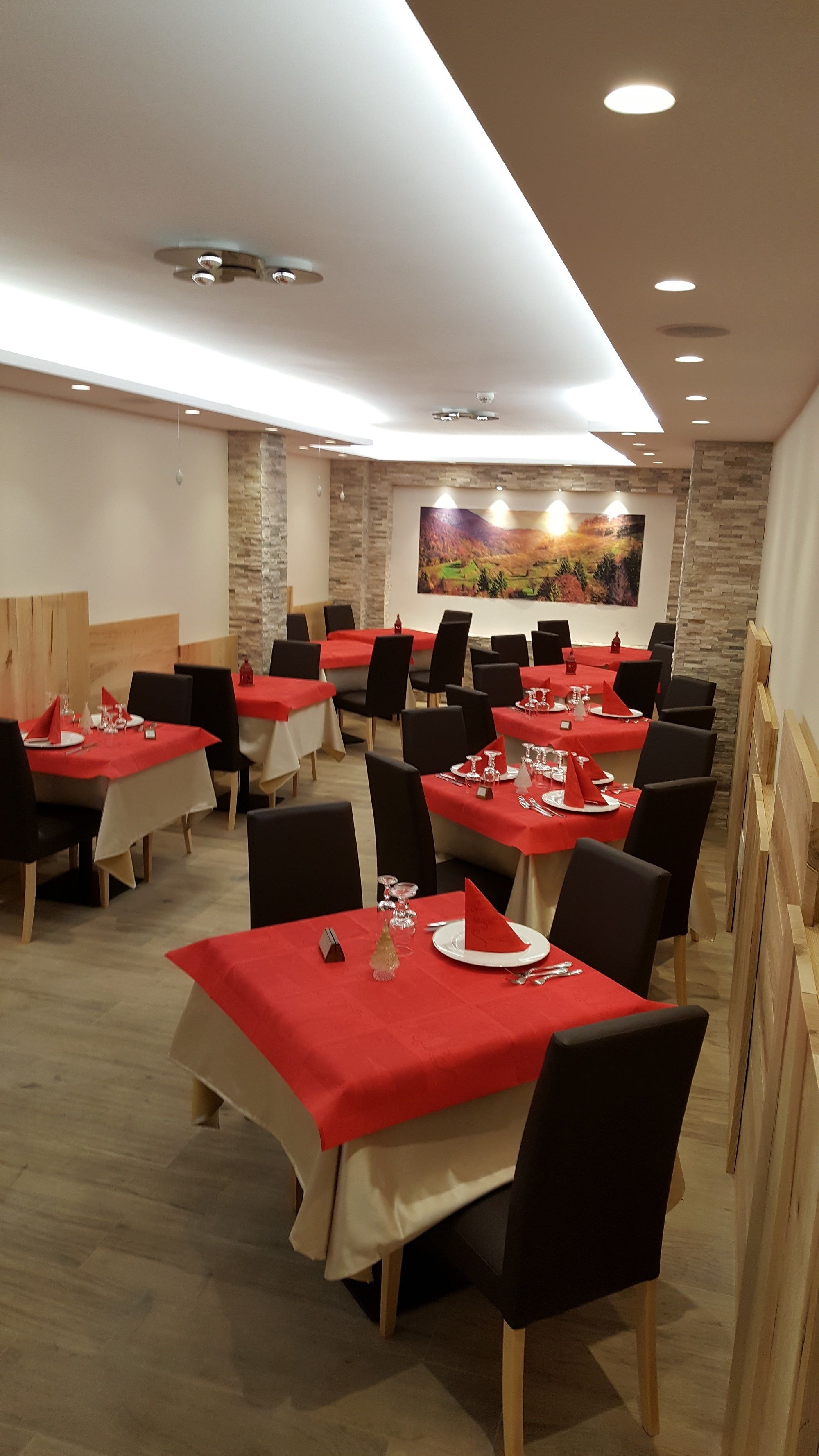Un espace repas avec plusieurs tables dressées, recouvertes de nappes rouges et agrémentées de chaises noires.
