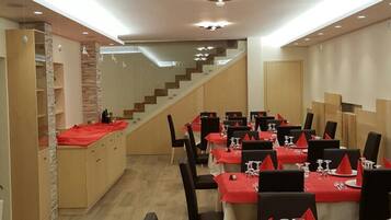 A dining area with multiple tables set for service, a staircase leading to an upper level, and a modern interior design.